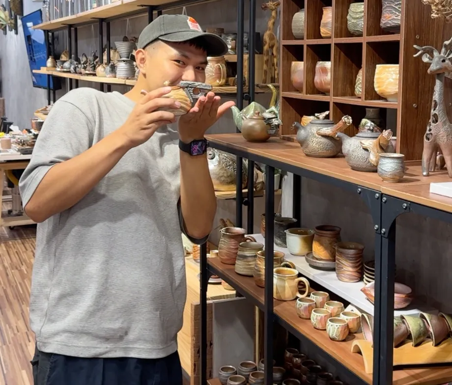 臻麟陶藝架上陳列的陶藝作品,柴燒茶壺、陶杯與陶碗一整排,手上拿著一只燒好的陶杯